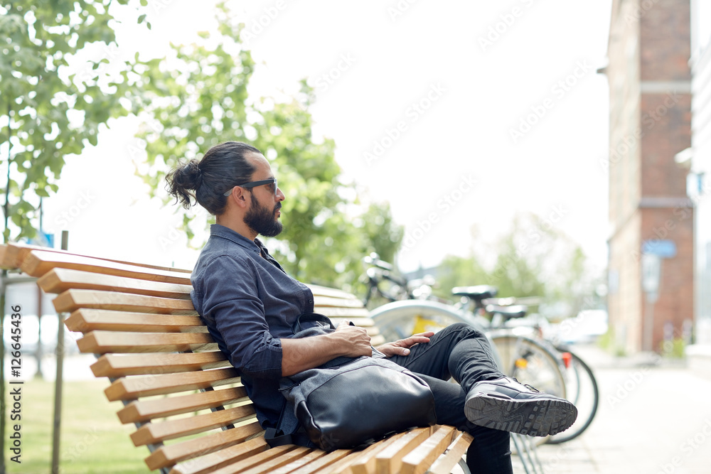 man with backpack sitting on city street bench man with backpack sitting on city street bench
