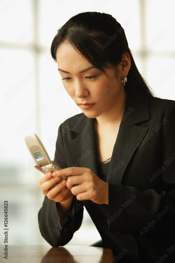 Young woman sitting at desk, using mobile phone Young woman sitting at desk, using mobile phone