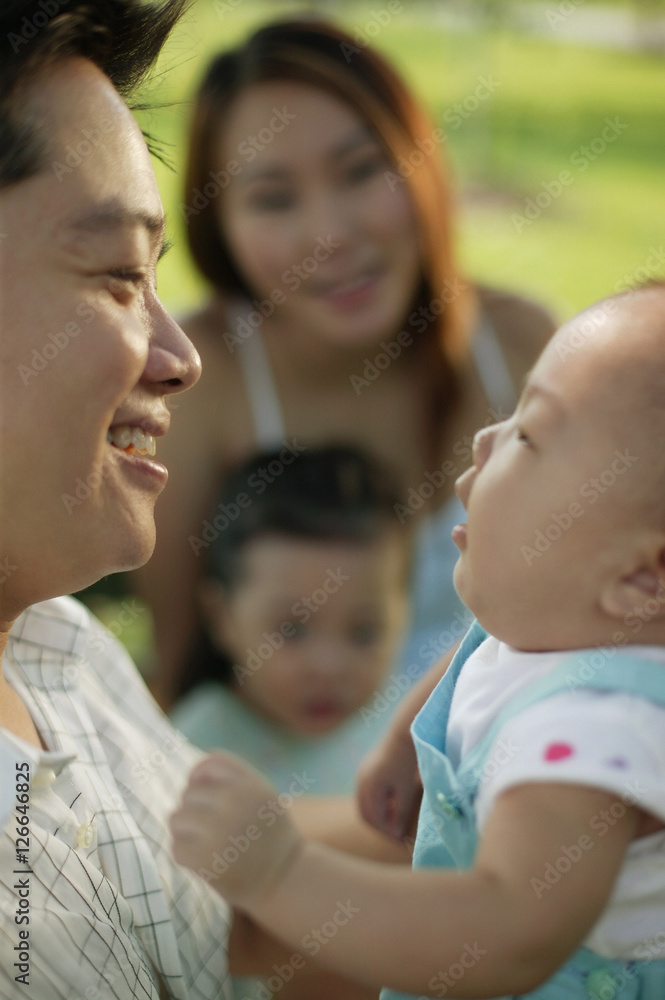 Father carrying baby, mother and young daughter in the background. Father carrying baby, mother and young daughter in the background.