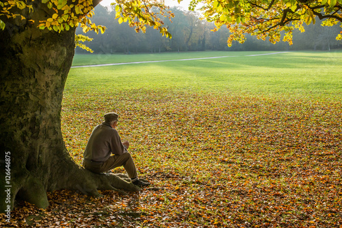 Uomo seduto sotto un albero in autunno all'Englischer Garten di Monaco di Baviera, Germania  photo
