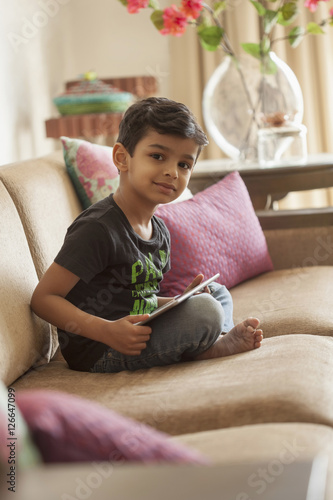 India, Little boy (4-5) sitting cross legged on sofa using digital tablet