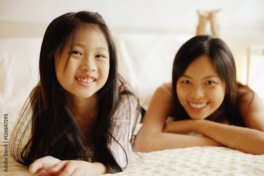 Mother and daughter lying on bed, looking at camera Mother and daughter lying on bed, looking at camera
