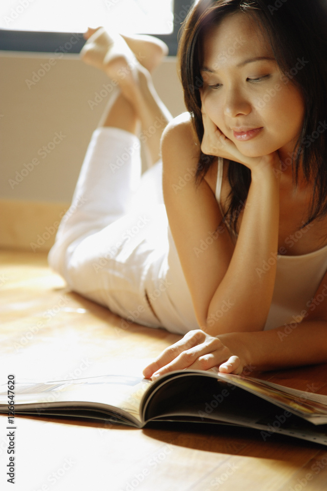 Young woman lying on floor reading magazine. Young woman lying on floor reading magazine.