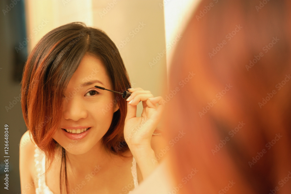 Woman putting on mascara, looking at mirror