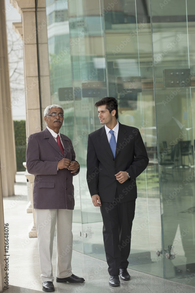 India, Senior and junior businessmen talking outside office building India, Senior and junior businessmen talking outside office building