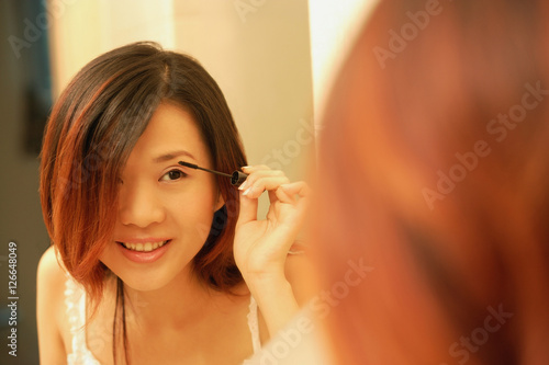 Woman putting on mascara, looking at mirror