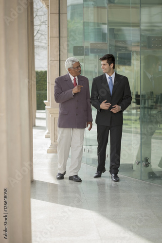 India, Senior businessman talking to junior businessman outside office building