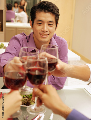 Friends toasting wine glasses across dinner table, over the shoulder view
