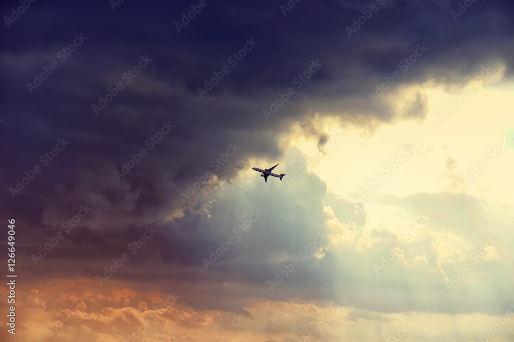 Naklejka premium The airplane passenger jet fly right in to the dark clouds just before storm. Colorful sunset rays. Emergency concept.