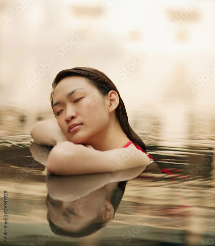 Young woman, at edge of swimming pool, eyes closed
