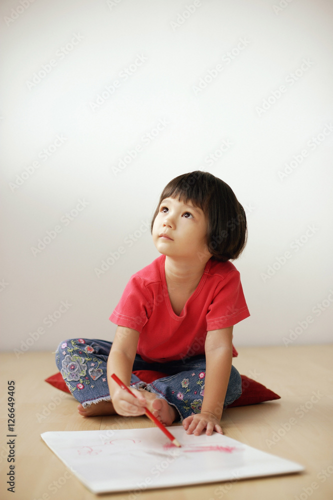 Young girl drawing on drawing pad, looking up