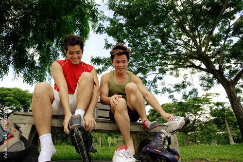 Photography Two men on park bench, putting on roller blades