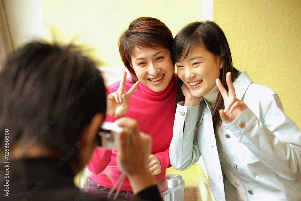Young man holding camera, two women posing for picture, making peace sign Young man holding camera, two women posing for picture, making peace sign