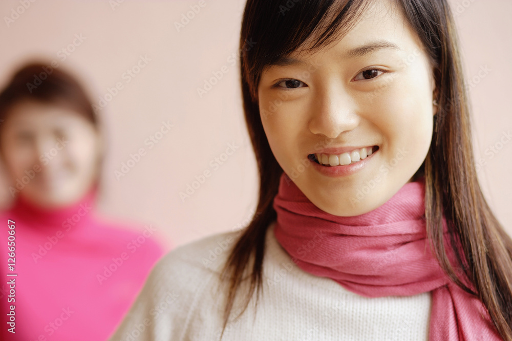 Young woman with scarf smiling, another woman in background Young woman with scarf smiling, another woman in background