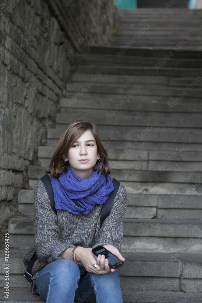 smiling girl in a blue scarf sitting on stone stairs outdoors