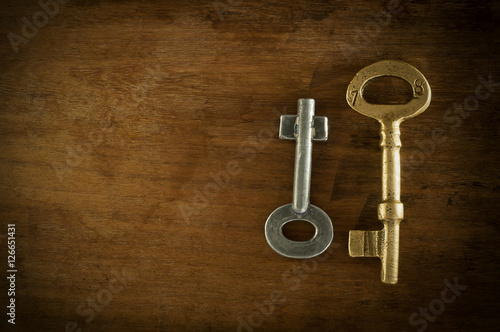 Old two keys placed on a wooden floor low key light.