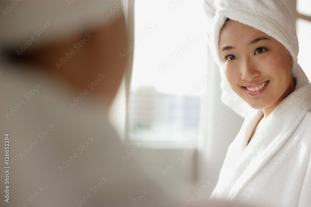Young woman looking at mirror, towel wrapped around her head Young woman looking at mirror, towel wrapped around her head