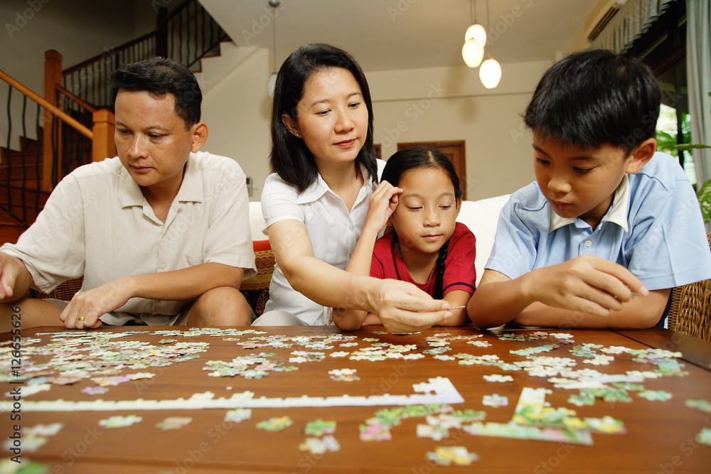 Family in living room, sitting side by side, working on jigsaw puzzle Family in living room, sitting side by side, working on jigsaw puzzle