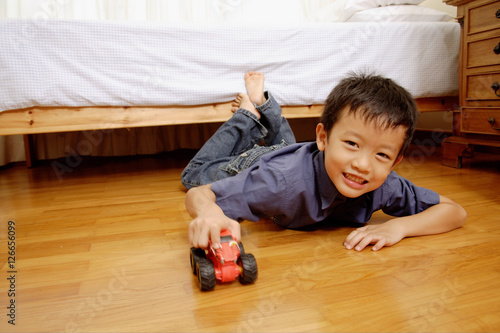Young boy lying on floor with toy car, looking at camera
