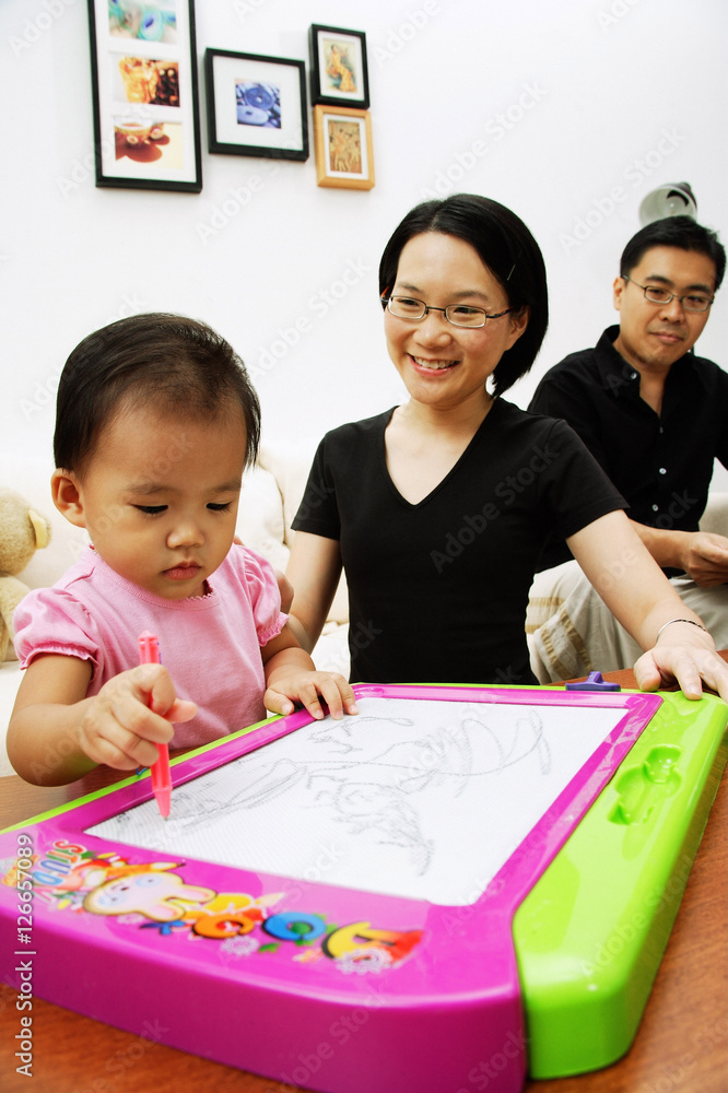 Young girl drawing on magnetic block, parents watching her Young girl drawing on magnetic block, parents watching her
