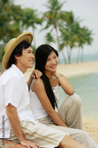 Couple sitting on beach, looking away