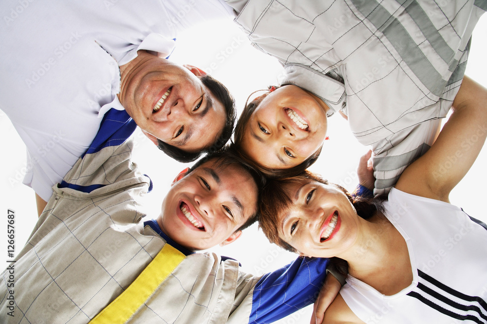 Fototapeta premium Family of four standing in a circle, arms around each other, looking down at camera