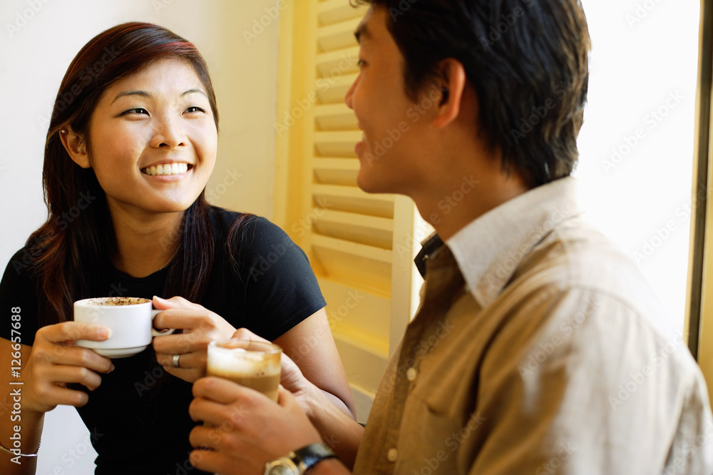 Couple sitting, holding coffee cups, side by side Couple sitting, holding coffee cups, side by side