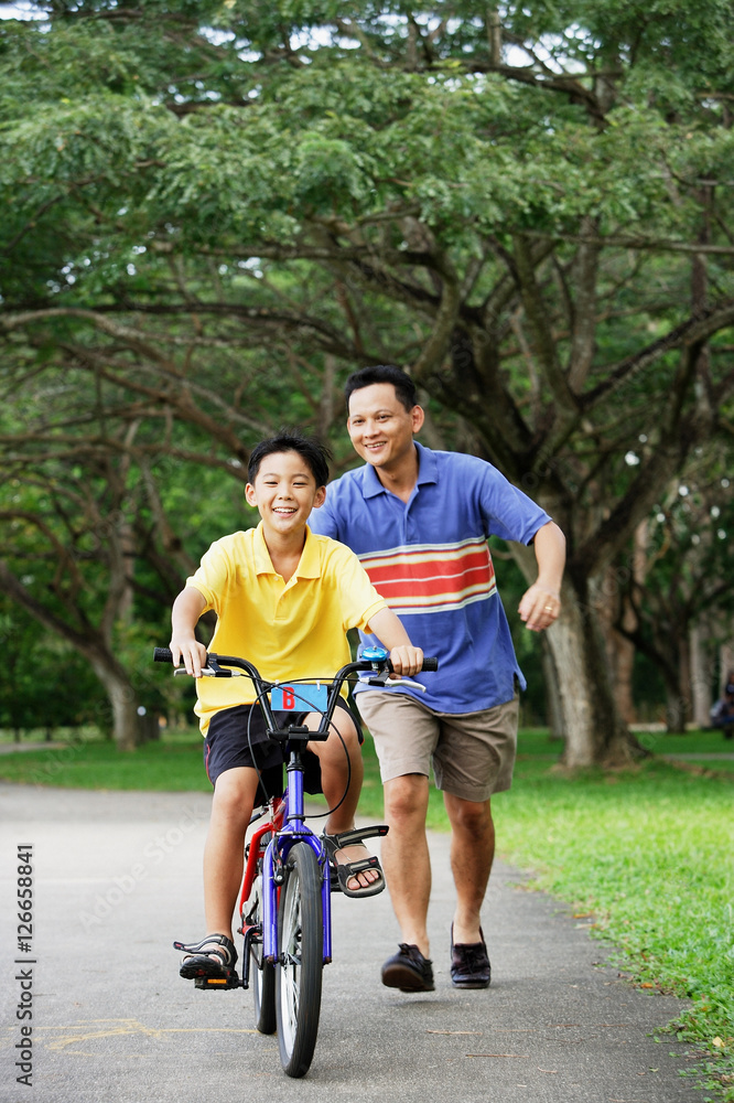Boy on bicycle, father running behind him, smiling Boy on bicycle, father running behind him, smiling