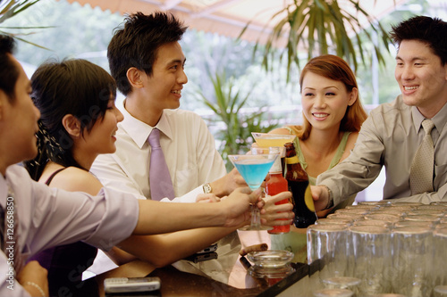 Young adults at bar counter toasting with drinks
