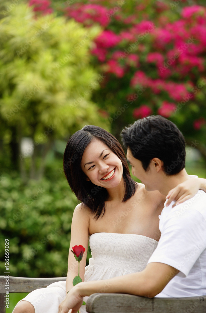 Fototapeta premium Couple sitting on park bench, looking at each other