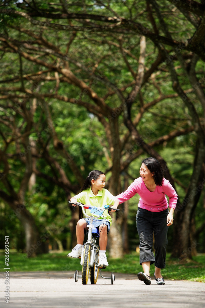 Girl cycling, mother walking next to her