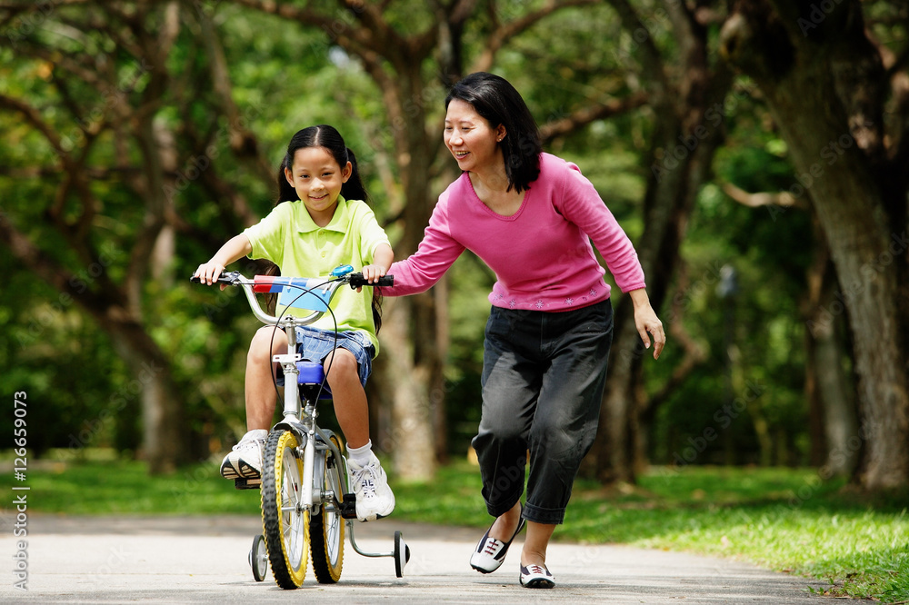 Girl on training bicycle, mother guiding her