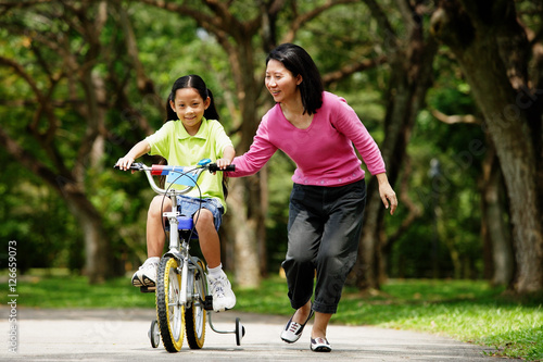Obraz na płótnie Girl on training bicycle, mother guiding her w salonie