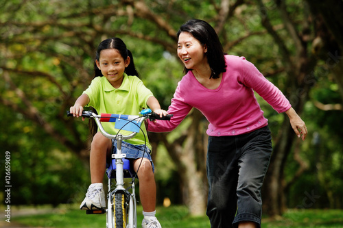 Girl on cycling, mother next to her, holding her