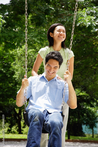 Man sitting on swing, woman standing behind him © Alexander