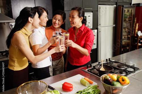 Women in kitchen, holding wine glasses, toasting