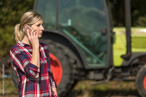 female farmer with tractor using mobile phone