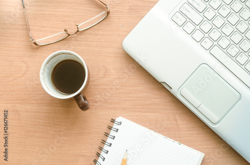 Laptop, cup of coffee, glasses and notebook on the desktop