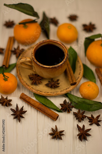 Small white cup of coffee, cinnamon sticks, star anise and mandarin on white wooden background