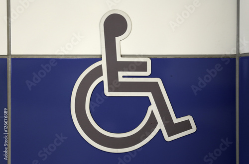 Grey wheelchair sign on the a white and blue wall. Public restroom signs with a disabled access symbol.