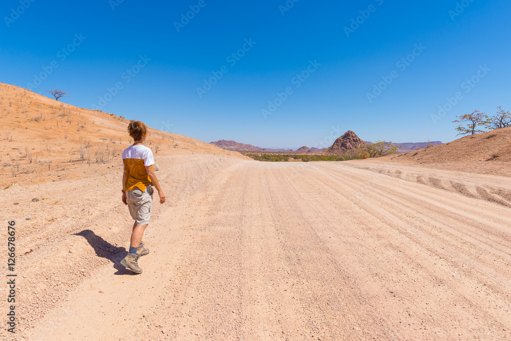 Tourist walking on 4x4 road crossing the colorful desert at Twyfelfontein, in the majestic Damaraland Brandberg, scenic travel destination in Namibia, Africa.