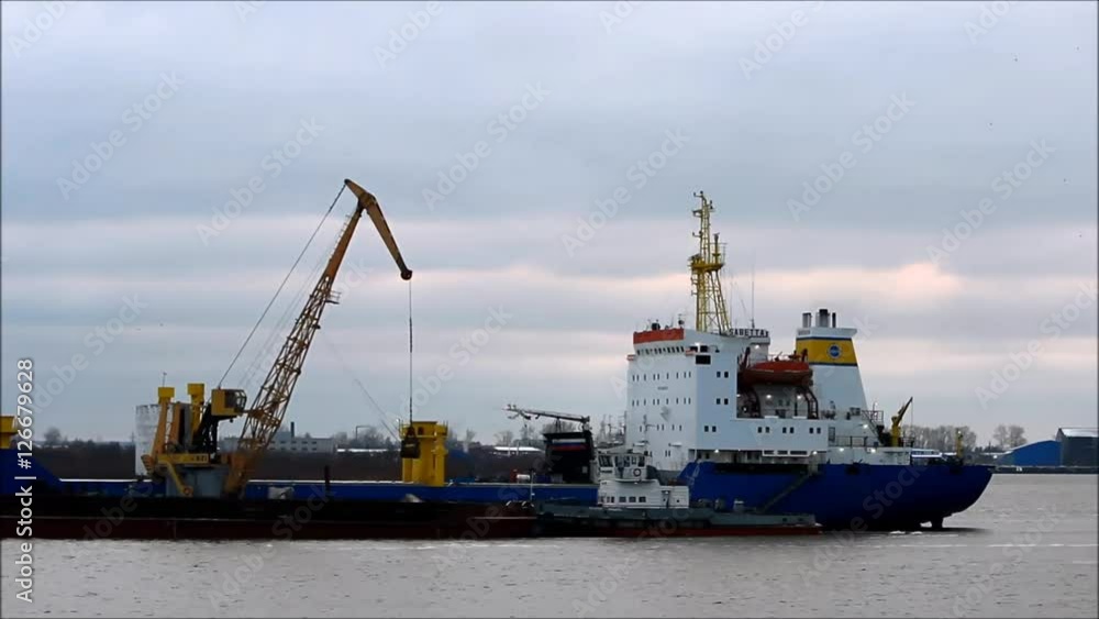 the process of loading coal from the barge to the ship on the river with the help of the port cargo crane. the process of loading coal from the barge to the ship on the river with the help of the port cargo crane.