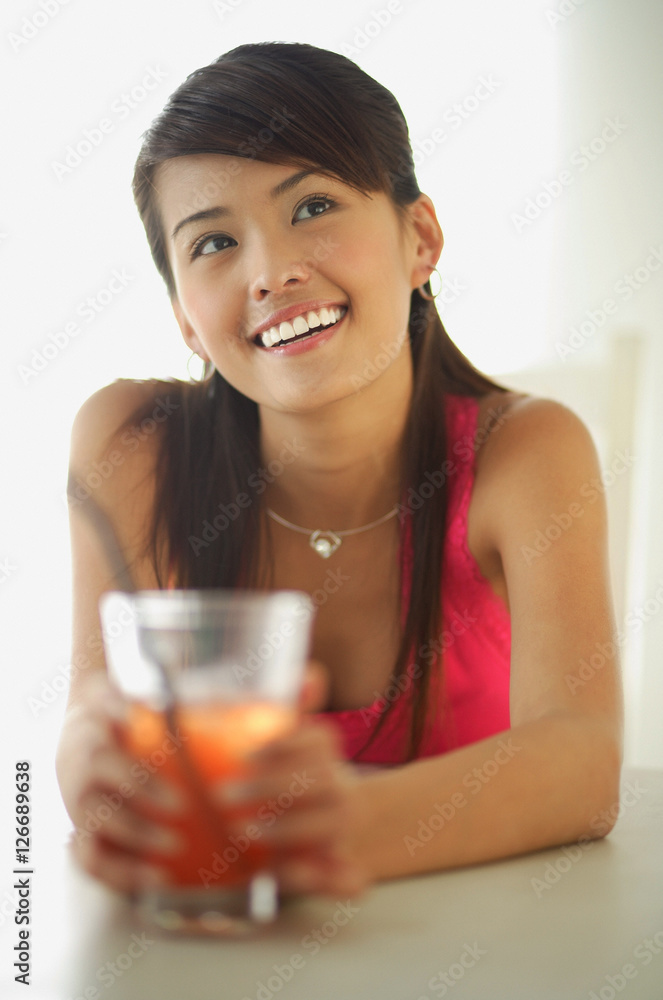 Woman sitting at table, holding drink, looking away, smiling Woman sitting at table, holding drink, looking away, smiling