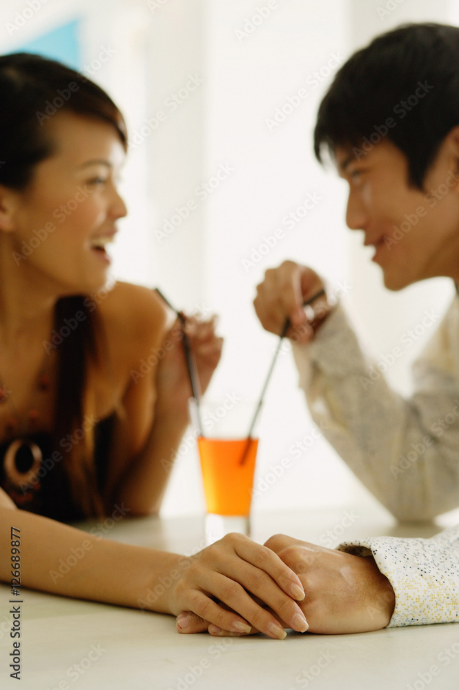 Couple sharing one drink, sitting face to face, holding hands Couple sharing one drink, sitting face to face, holding hands