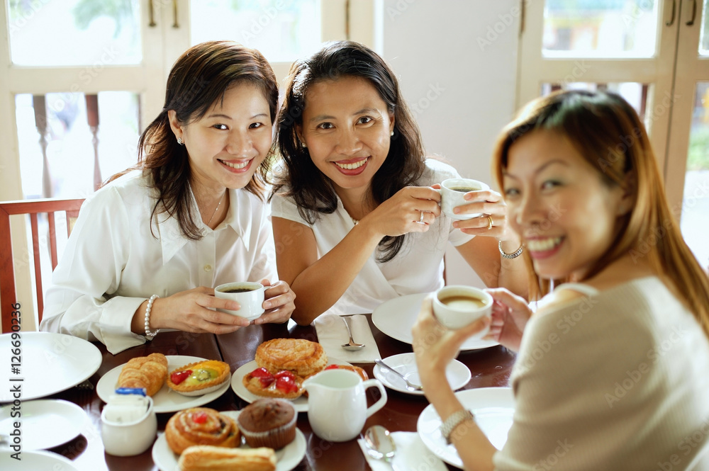 Three women having tea at cafe, smiling at camera