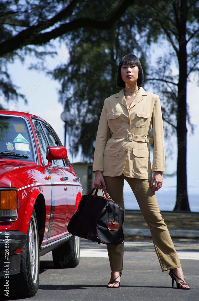 Woman standing by car, carrying bag