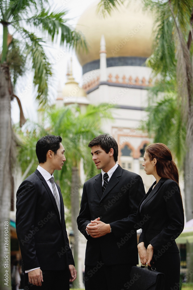 Two businessmen and one businesswoman standing, having a discussion, mosque in the background Two businessmen and one businesswoman standing, having a discussion, mosque in the background