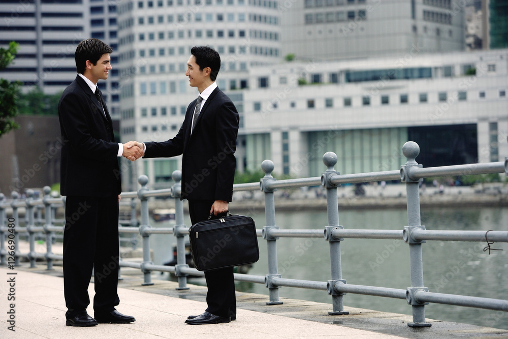 Two businessmen shaking hands, buildings in the background