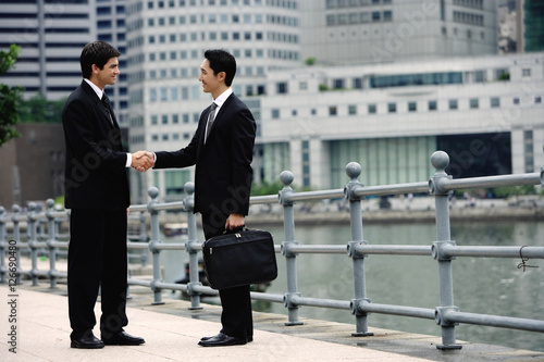 Obraz na płótnie Two businessmen shaking hands, buildings in the background w salonie