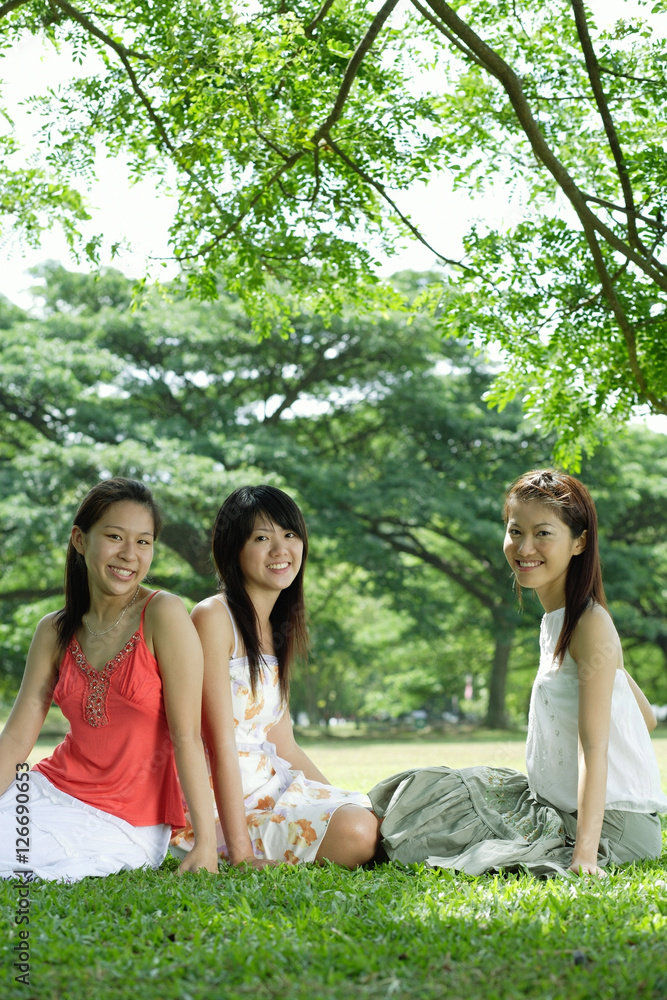 Fototapeta premium Young women sitting on grass, smiling at camera